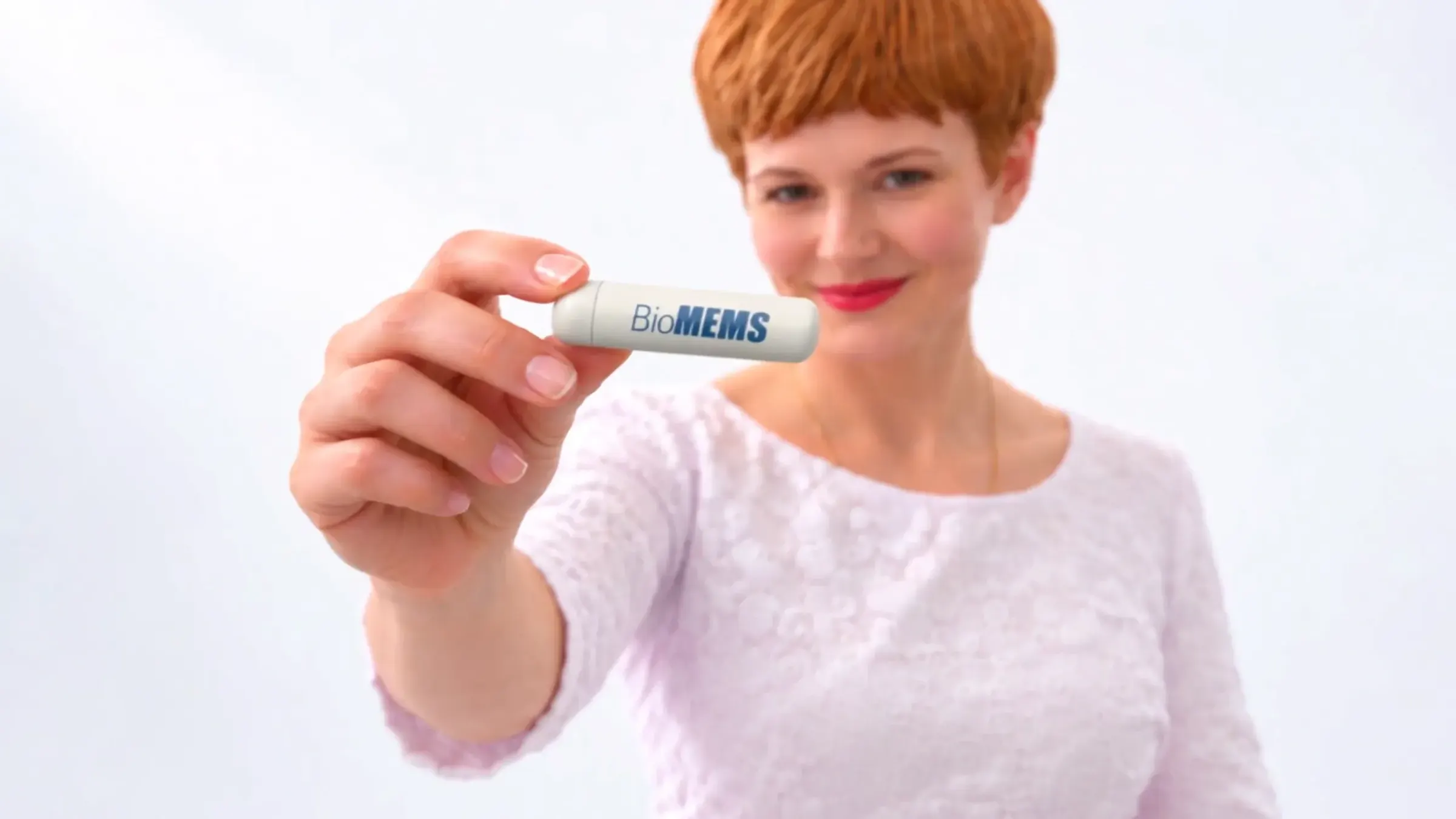 A woman holds up the small white BioMEMS cartridge toward the camera.